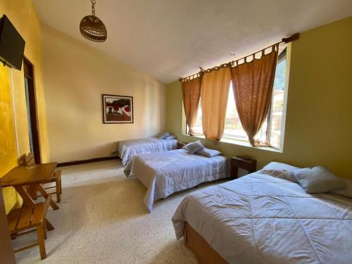a bedroom with two beds and a desk and two windows at HOTEL IXBALANQUE in La Aurora