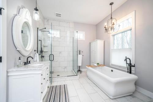 La salle de bains blanche est pourvue d'une baignoire, d'un lavabo et d'un miroir. dans l'établissement Large luxurious home - 2 blocks from nearest public beach - Private heated pool!, à South Haven