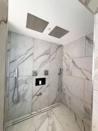 La salle de bains est pourvue d'une douche et de murs en marbre blanc. dans l'établissement Appartement 50m2 spa privé, à Saint-Aygulf