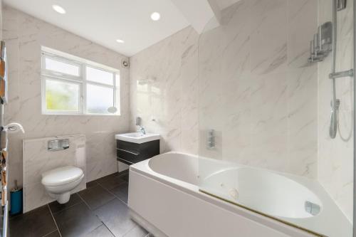 baño blanco con bañera y aseo en Barnet Serviced Accommodation - Elegant 5-Bedroom Home, Just a 7-Minute Stroll from High Barnet Station - Book Your Stay Today!", en New Barnet