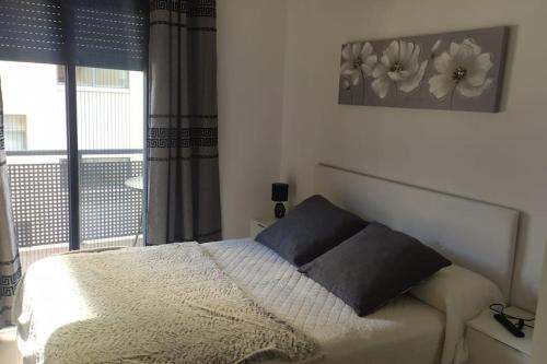 ein Schlafzimmer mit einem Bett und einem Fenster mit Blumen an der Wand in der Unterkunft Apartamento nuevo con piscina y amplio balcon in Sant Carles de la Ràpita
