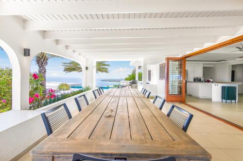 ein langer Holztisch und Stühle in einem Raum mit Blick auf das Meer in der Unterkunft Exclusive 10-Guest Seaview Villa in Gated Community with Pool & Private Beach Access in Willibrordus