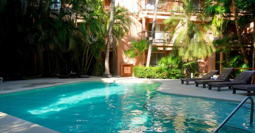 a swimming pool in front of a building with palm trees at Tukan Hotel Playa del Carmen in Playa del Carmen