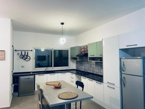 a white kitchen with a table and a refrigerator at Dar Maya in Salakta