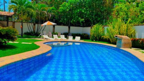 a swimming pool in a yard with chairs and an umbrella at Pousada Villa Mariposa in Beberibe