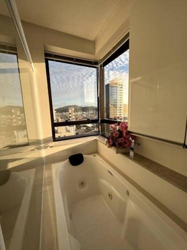 uma grande banheira branca num quarto com janelas em Apartamento no centro, com vista mar e Cristo Luz em Balneário Camboriú