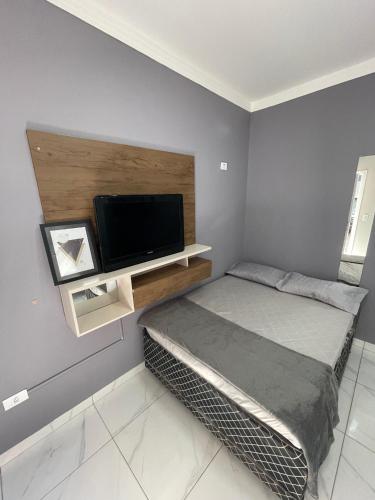 a bedroom with a bed and a flat screen tv at Kitnet Luz do Mar in Maringá