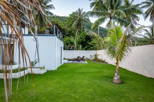 a yard with a palm tree and a white wall at Secret Pearls by Matira Beach in Bora Bora