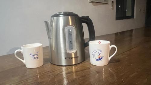 three coffee mugs sitting on a table with a coffee pot at 永勝客棧 in Manzhou