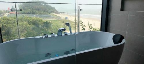 a bath tub in a bathroom with a view of a beach at Flamingo Ibiza Hải Tiến in Nam Khê