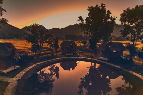 a bridge over a pond with a sunset in the background at The Countryside Pai in Pai