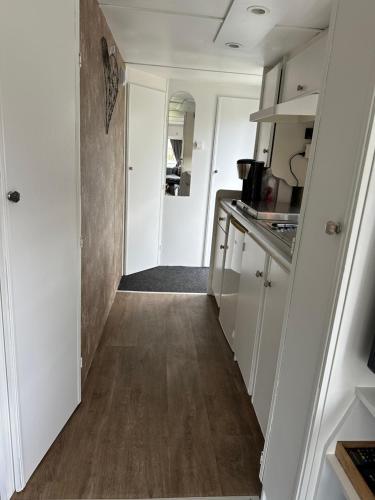a kitchen with white cabinets and a wooden floor at Stacaravan 130 De Tien Heugten in Schoonloo