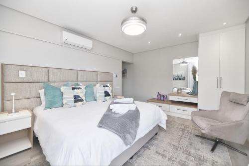 a white bedroom with a bed and a chair at Cliff Haven in Struisbaai