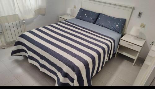 Port de la Selva apartament في بورت دي لا سيلفا: سرير مع لحاف مخطط باللون الأزرق والأبيض في غرفة النوم