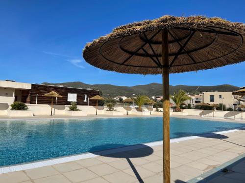 Un grand parasol est installé à côté de la piscine. dans l'établissement Villa 4 à 6 personnes dans résidence avec piscines proche plage, à Belgodère