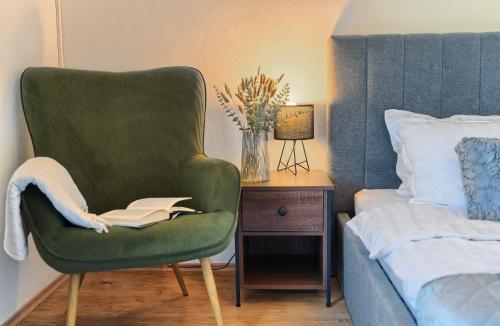 a green chair with a book on it next to a bed at RELAX apartment Split area with private jacuzzi on terrace with mountain view in Srinjine