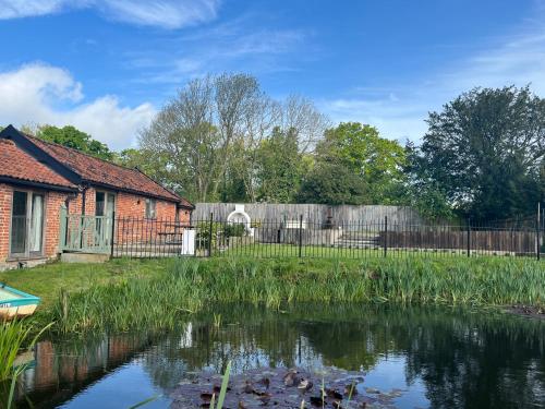 a house with a pond in front of a fence at Oak Grange holiday cottage in Hoxne