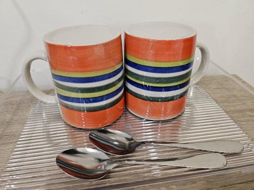 two colorful coffee mugs and a spoon on a table at The Blue Guest House, WiFi, Free Parking, Aulong in Taiping