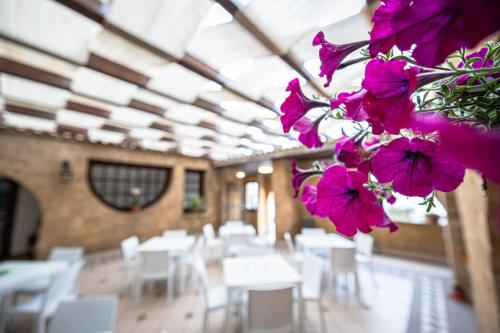 Cette chambre comprend des tables, des chaises blanches et des fleurs violettes. dans l'établissement La Rosa Hotel - Selinunte, à Marinella di Selinunte