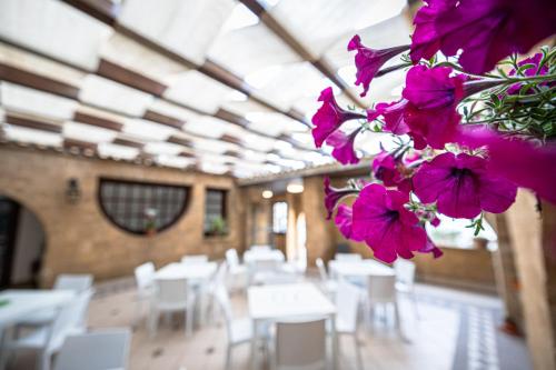 uma sala com mesas e cadeiras brancas e flores roxas em La Rosa Hotel - Selinunte em Marinella di Selinunte