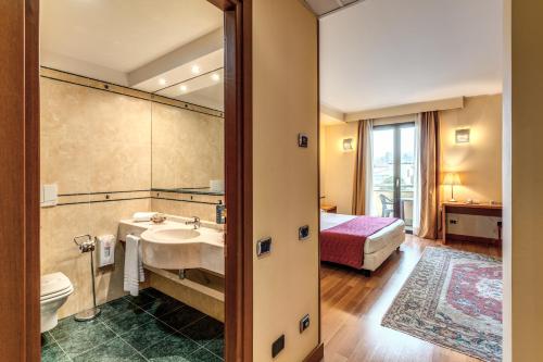 a bathroom with a sink and a toilet and a bed at Luna Hotel Lago Maggiore Arona in Oleggio Castello