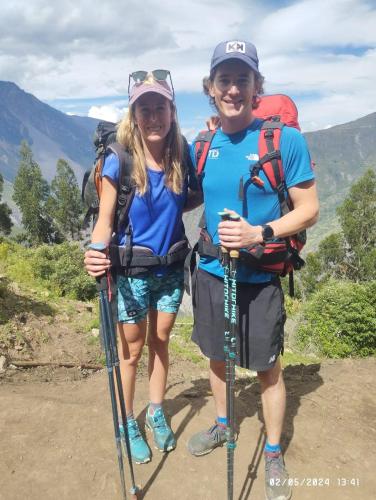 a man and woman standing on a trail with trekking poles at the wooden house choquequirao in Cachora