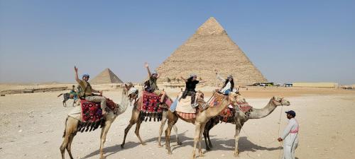 Pyramids Temple Guest House في القاهرة: مجموعة من الناس يركبون على الجمال امام الاهرامات