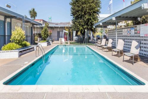 a blue swimming pool with chairs and a building at Travelodge by Wyndham San Francisco Airport North in South San Francisco