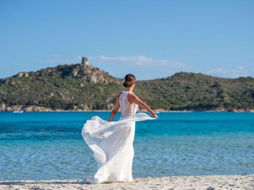 a woman in a wedding dress walking on the beach at Almar Timi Ama Resort & Spa in Villasimius