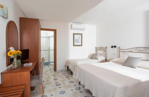 a hotel room with two beds and a desk and a television at Hotel Il Girasole in Anacapri