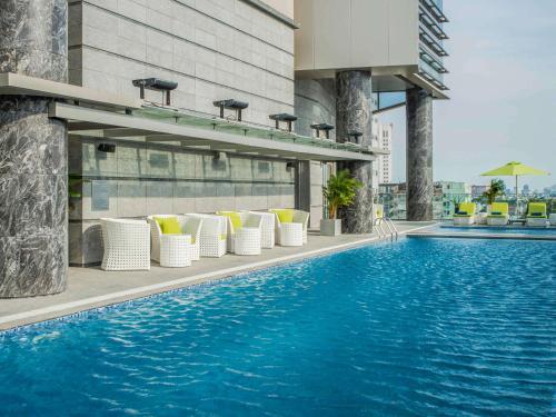 a swimming pool with white chairs and a building at Pullman Saigon Centre in Ho Chi Minh City
