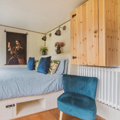 a bedroom with a bed and a blue chair at The Hideaway at Hidden Wood Glamping in Corsley