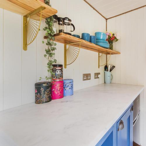 a kitchen counter with blue cabinets and shelves at The Hideaway at Hidden Wood Glamping in Corsley