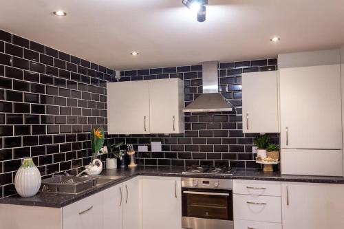 a kitchen with white cabinets and black tiles on the wall at 4 Bed complete Home in Edinburgh Near Airport in Edinburgh