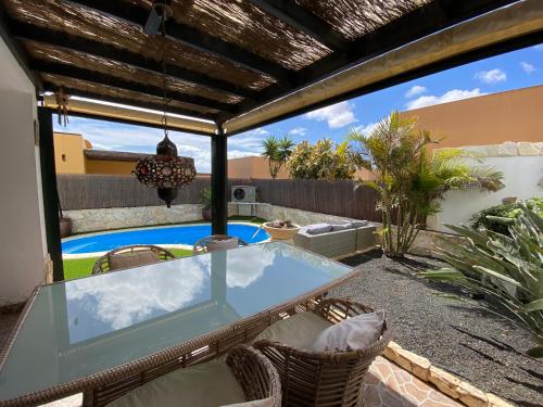 a patio with a glass table and chairs and a swimming pool at Casa Rosalía in Corralejo