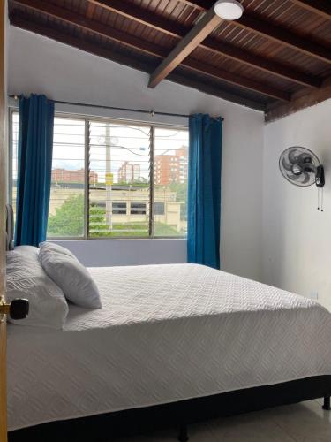 a bedroom with a bed with blue curtains and a window at Hotel Mallorca Estadio, Medellin in Medellín