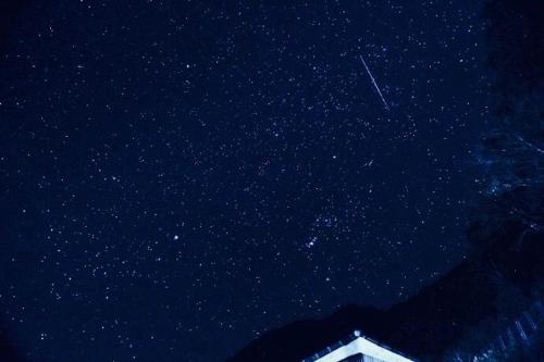 a starry night with a building and a plane in the sky at ラコマハウス in Takinohai