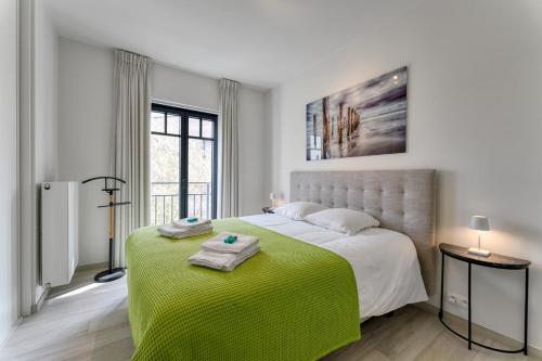 een witte slaapkamer met een groot bed met een groene deken bij Zonnig Luxueuze Appartementen La Coronne in Knokke-Heist