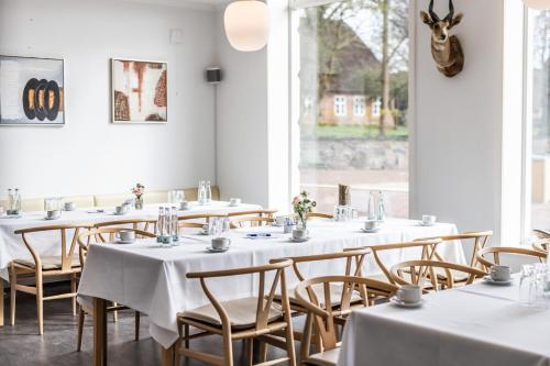 Marsk Hotellet في Højer: صف من الطاولات في غرفة مع طاولات وكراسي بيضاء