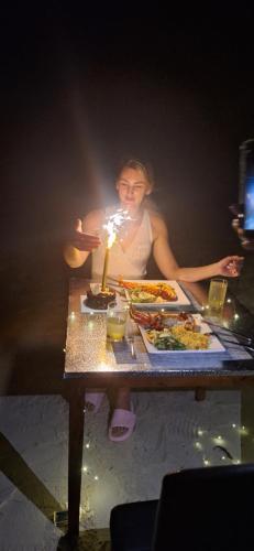 a woman sitting at a table with a table with food at Alesara Guest House in Thoddoo