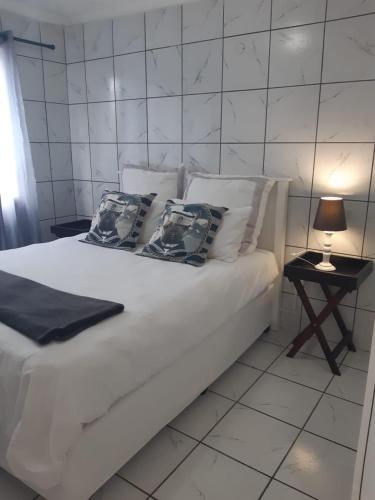 Cama blanca con almohadas y mesa con lámpara en The Getaway, en Port Alfred