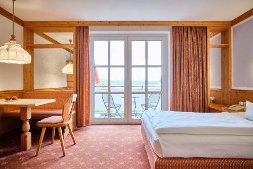 a hotel room with a bed and a table and a balcony at Strandhotel Seehof in Langlau