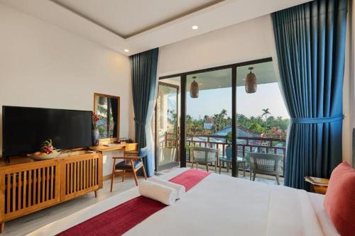 a bedroom with a bed and a television and a balcony at Én Mansion Hoi An in Hiếu Nhơn