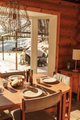 a wooden table with chairs and a dining room with a window at Le Petit Domaine Caché - Lac-Simon in Lac-Simon