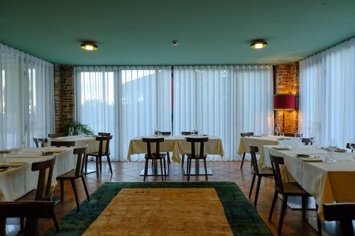 un restaurante con mesas y sillas blancas y ventanas en Le Badie Wine Resort, en Rosazzo