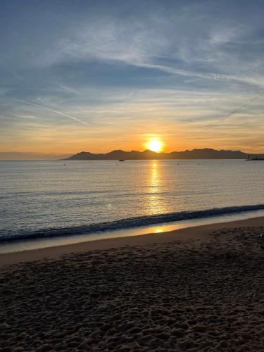 a sunset on the beach with the sun setting over the water at Cannes, la Croisette, Palais Miramar in Cannes