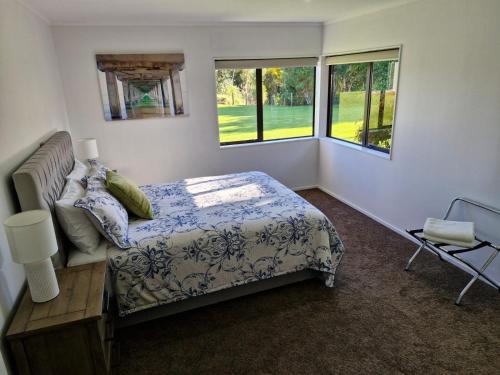 a bedroom with a bed and two windows at Palms on Bruntwood in Tamahere