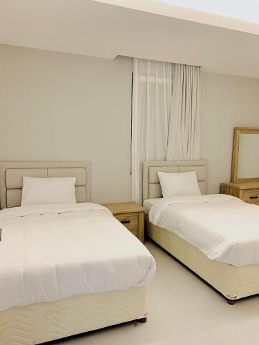 2 camas en una habitación de hotel con sábanas blancas en Iveria Hotel Apartments en Ḩayl Āl ‘Umayr
