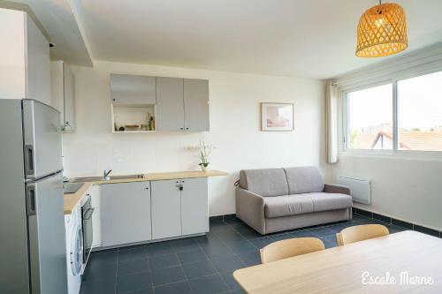 a kitchen with a refrigerator and a table and a chair at escale-marne fr - 11 - Appartement entier, 4 pers, 10mn metro 8, RER A, Parking rue Gratuit, Cuisine Équipée, Grand lit haut de gamme, Matelas Eve Sleep, 1er étage in Maisons-Alfort