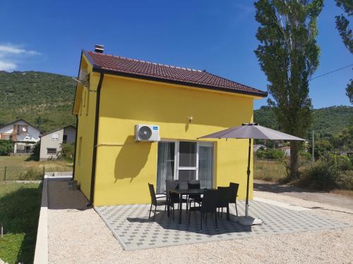 a yellow house with a table and chairs and an umbrella at Žuta kuća in Grude